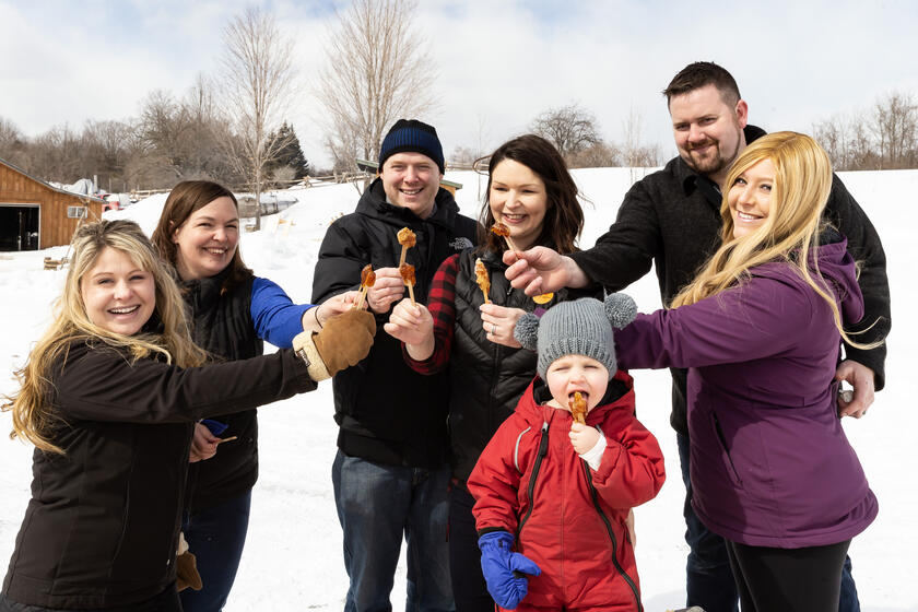 People smiling in winter and holding maple syrup taffy