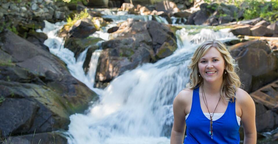 happy woman standing in front of waterfall