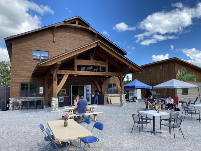 Haliburton Highlands Brewing back patio; several tables and chairs with a few people sitting at them, large brown building and blue sky in background