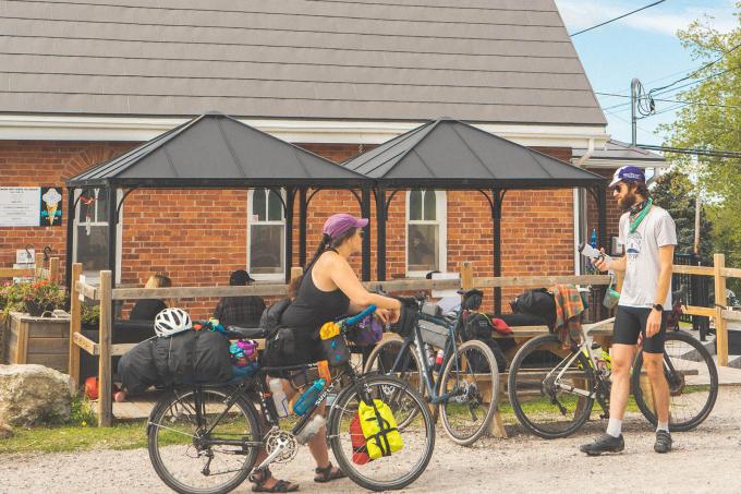 Two people stand with bicycles in front of Cardinal Cafe.