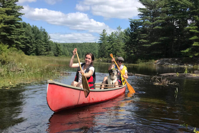 two smiling people paddling red canoe with small dog between them