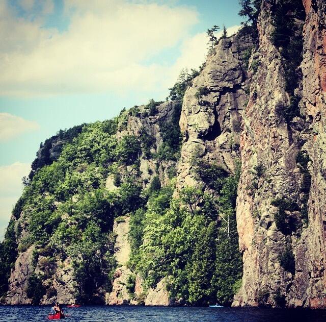 A couple paddling a canoe on a lake beneath a large outcropping.